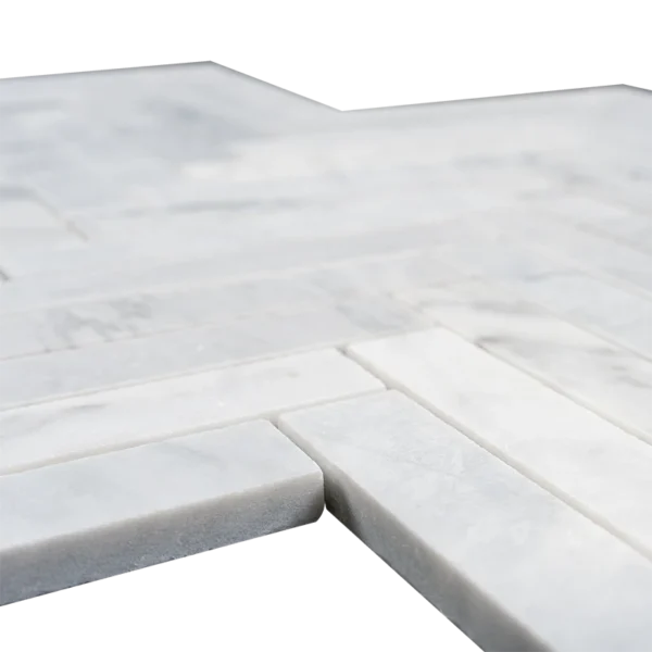 A detailed close-up of the 1x6 honed Carrara marble mosaic tile arranged in a herringbone pattern. The matte-finished white tiles with delicate gray veining showcase their natural texture and thickness, highlighting the clean edges and fine craftsmanship. Ideal for modern and classic designs.