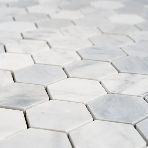 Close-up of 2-inch honed Carrara White marble honeycomb mosaic tiles with hexagon shape and soft matte finish.