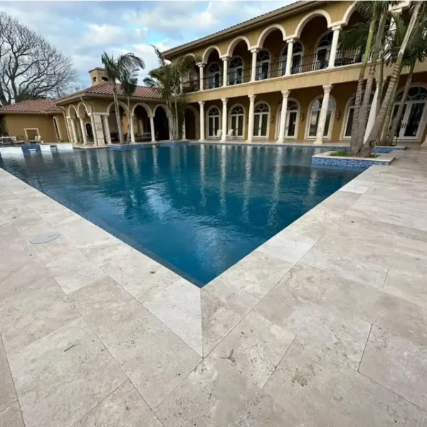 Ivory travertine pavers around a luxury pool deck — light beige tones with tumbled, non-slip finish