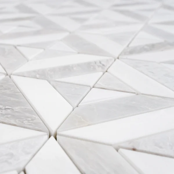Detailed perspective highlighting the three-dimensional relief of the white and light gray geometric marble mosaic tile sheet, showing the varying heights and sharp edges of the tiles.