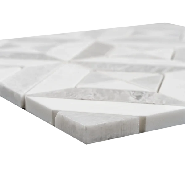 Low-angle view of a white and light gray geometric marble mosaic tile sheet showing its raised relief and precise layout.