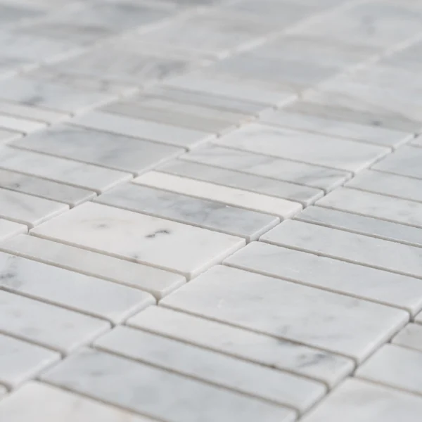 Angled close-up of the Carrara strip linear mosaic showing polished surfaces, tight joints, and subtle gray veining.