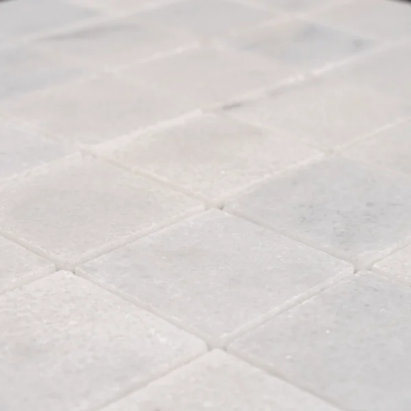 Detailed macro shot of Milas White 2x2 polished marble mosaic tiles, emphasizing the reflective shine and fine marble grain.