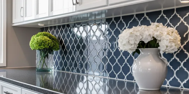 Blue arabesque mosaic tile kitchen backsplash with white cabinets and dark countertop
