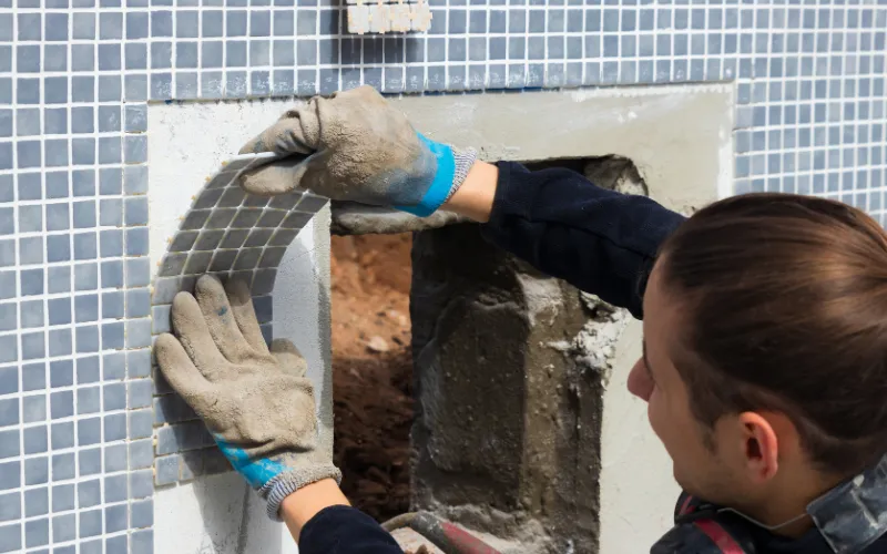 Worker installing mesh mounted mosaic tile sheet on wall during tile installation process