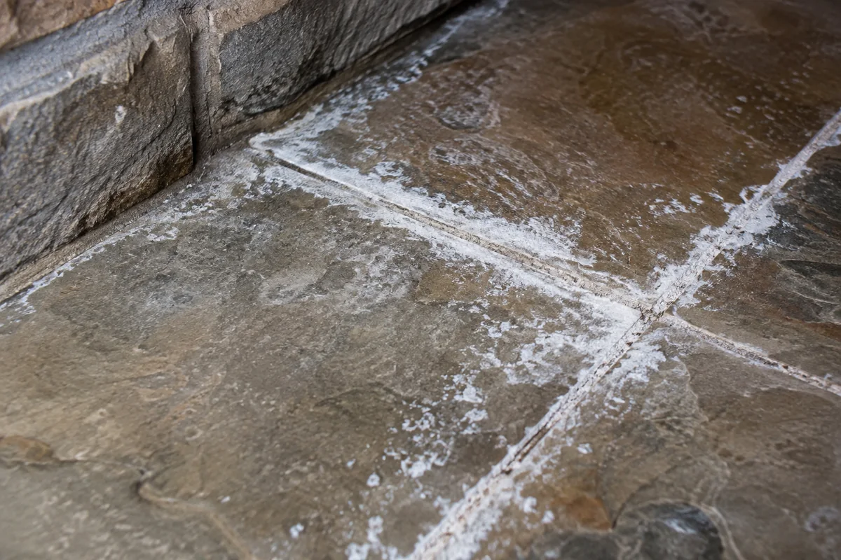 White crystalline residue gathered along grout joints on a natural stone tile floor