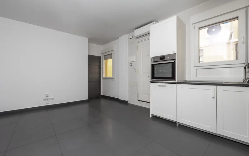 Empty apartment kitchen with white cabinets, white brick walls, gray countertop, and gray porcelain tile flooring